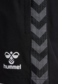 Zwarte stof met wit hummel bijenlogo en merknaam, naast een verticale getextureerde streep met terugkerende chevronpatronen.