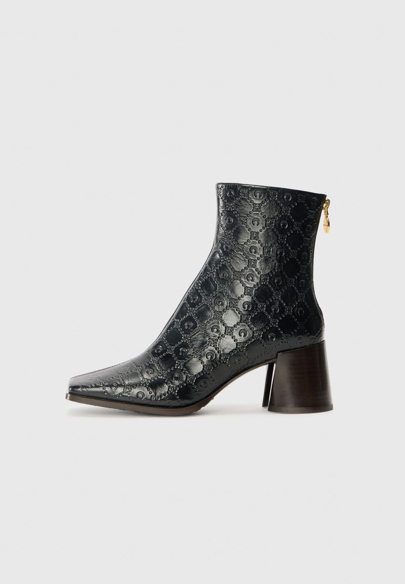 Svart ankelboot med en texturerad läderutsida med ett blommönster, spetsig tå och en kraftig klack. Sidozip med guld detaljer.