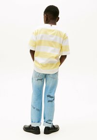 Gestreepte gele en witte short-sleeve shirt, blauwe spijkerbroek met grafische prints, en zwarte schoenen met een ronde neus.