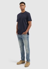 Marine crew-neck t-shirt, korte mouwen. Lichtblauwe jeans, vervaagd op de dijen. Beige schoeisel met veters, rubberen zool. Eenvoudig ontwerp, geen zichtbare patronen.