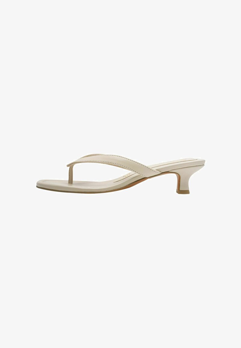 Sandale tongs beige avec une fine lanière. Présente un talon bas et incurvé ainsi qu'une finition lisse et brillante. Esthétique minimaliste.