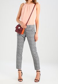 Blusa sin mangas de color rosa claro con escote plisado, pantalones a medida de cuadros grises, y un pequeño bolso bandolera burdeos-anaranjado. Sandalias negras con tacón.