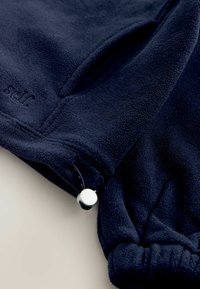 Pull à capuche en polaire bleu marine avec tissu texturé, fermeture à cordon de serrage et détails en métal argenté. Présente un petit logo sur le tissu.