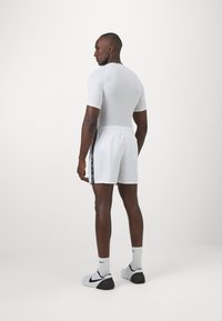 Pantalones cortos deportivos blancos con rayas laterales negras, combinados con una camiseta ajustada blanca de manga corta. Tejido suave, cinturilla elástica, diseño minimalista.