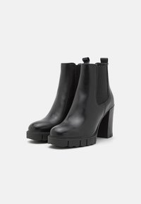 Botas de tobillo de piel negra con un tacón grueso, paneles laterales elásticos y una suela de goma texturizada. Acabado liso con un aspecto pulido.