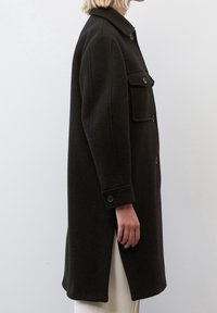 Cappotto in lana nera oversize con collo a camicia, due tasche frontali e polsini con bottoni; texture liscia; design lungo fino al ginocchio.