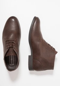 Botas de tobillo de cuero marrón con una textura suave, que cuentan con una puntera redondeada, diseño de cordones y un tacón bajo de goma.