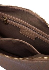 Bruine tas met rits aan de binnenkant, met een gladde textuur, een klein zakje, een logo-label en een stoffen voering met een subtiel patroon.