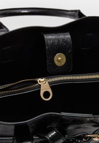 Intérieur d'un sac à main en simili cuir noir avec une fermeture éclair dorée, du matériel doré et un fermoir magnétique. Surface texturée et design spacieux.