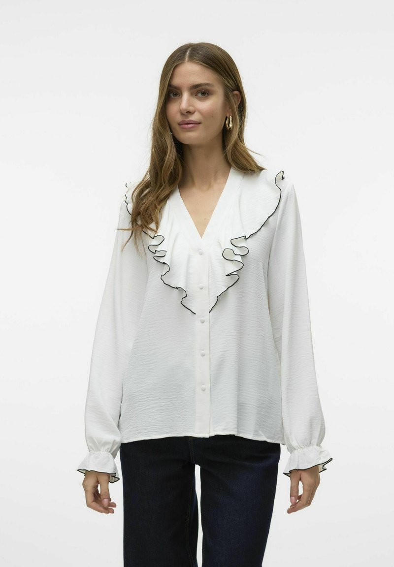 Blusa blanca con cuello volado bordeado en negro, que presenta un escote en V, cierre de botones en el frente y mangas largas con puños volados.
