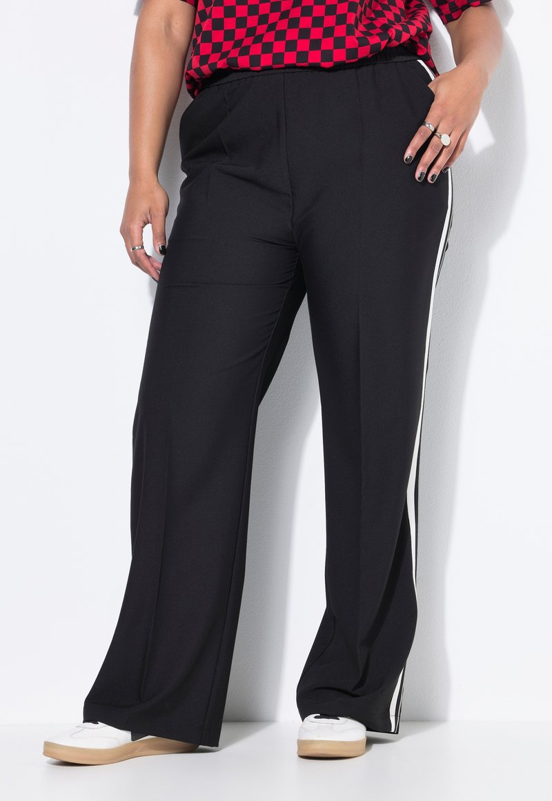 Zwarte wijde broek met een zachte textuur, voorzien van witte zijstrepen en een hoge taille. Gecombineerd met witte schoenen.
