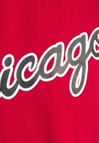 Tela de algodón rojo con texto en blanco y gris que dice "Chicago" en una fuente cursiva. El material tiene una textura suave.