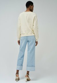 Sweatshirt crème avec épaules tombantes, associé à un jean ample bleu clair avec des ourlets retrouss�és. Le modèle porte des sandales à talons beiges.