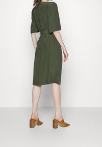 Knee-length olive green dress with short sleeves and a belted waist, paired with brown block-heeled sandals. Textured fabric.
