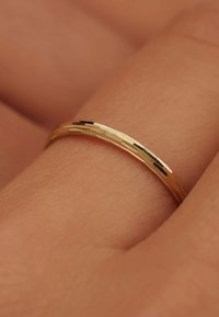 Bague en or avec une surface texturée, dotée d'un profil mince et de rainures subtiles, reposant sur une surface de couleur chair.