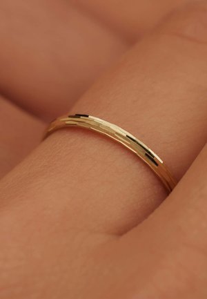 Bague en or avec une surface texturée, dotée d'un profil mince et de rainures subtiles, reposant sur une surface de couleur chair.