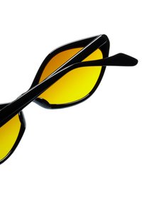 Černé sluneční brýle ve tvaru kočičích očí, se žlutě zabarvenými skly a elegantními černými obroučkami. Hladká textura bez viditelných akcentů nebo vzorů.