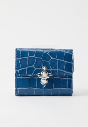 Portafoglio blu con texture a coccodrillo con emblema metallico argentato a forma di pianeta con una croce, su sfondo bianco.