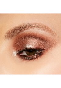 Close-up of an eye with warm, shimmery brown eyeshadow, defined lashes, and an arched eyebrow, set against smooth skin.