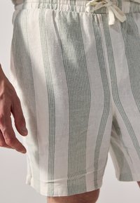 Shorts en lin à rayures verticales vert clair et blanches, avec une taille élastique et un détail de cordon de serrage.