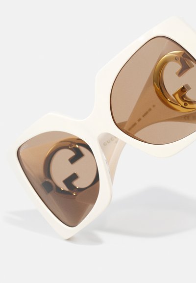 Gafas de sol blancas de gran tamaño con lentes de tono marrón, con un acento del logo doble G dorado en el interior de la montura. Acabado suave con forma geométrica.