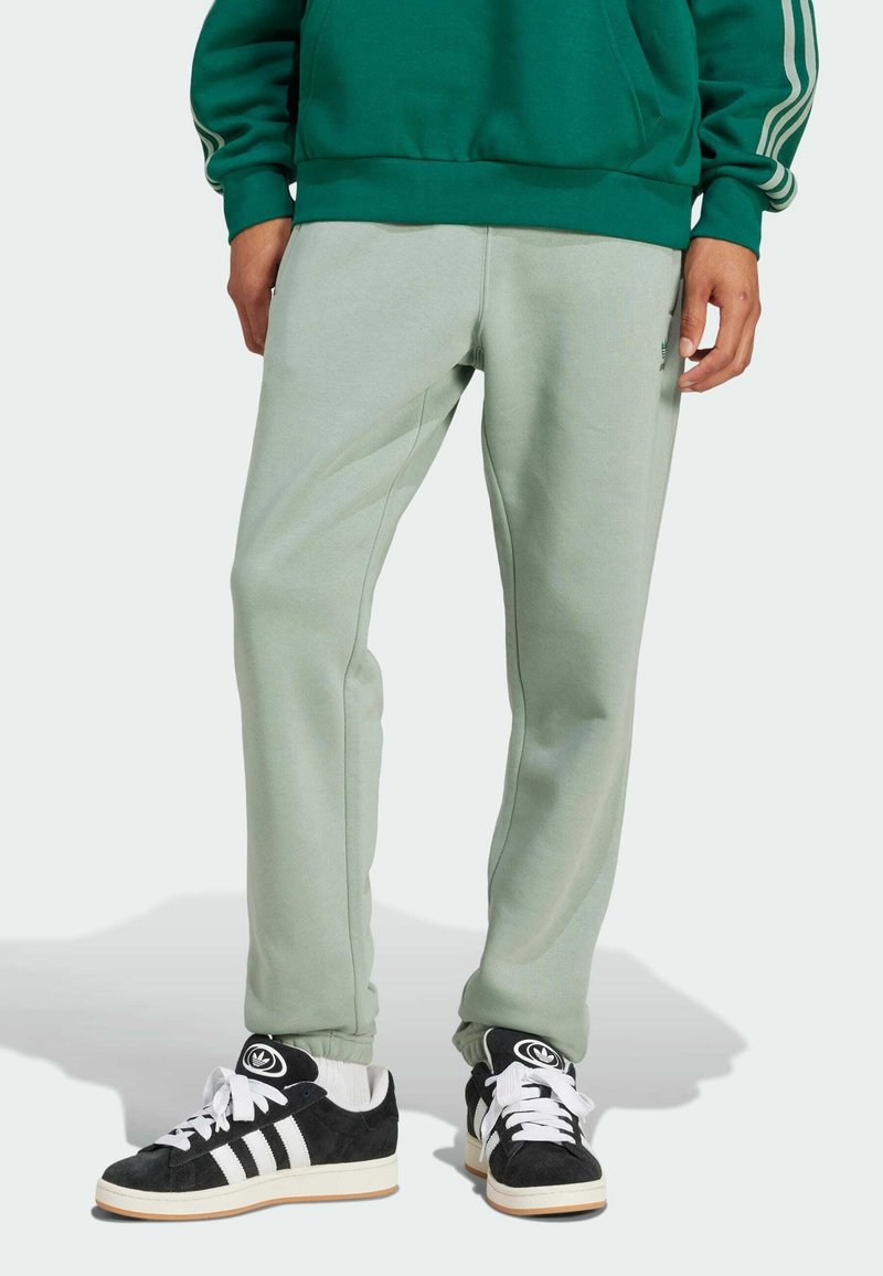 Ljusgröna mjukisbyxor har en avsmalnande design med elastiska Hände. Sammanförda med svarta och vita sneakers som visar strukturerade material och ränder.