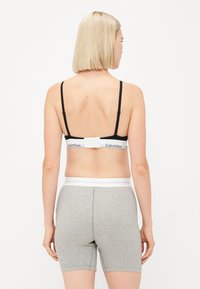Čierny bralet s nastaviteľnými popruhmi a bielym značkovým pásom, spárovaný so šedými rebrovanými šortkami s bielym elastickým pásom.