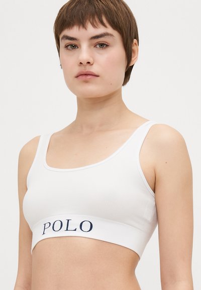 Bela bralette iz bombaža z ribasto teksturo, ki ima na elastičnem traku mornarsko modro "POLO" logo. Preprost dizajn, krožen izrez, tanke naramnice.