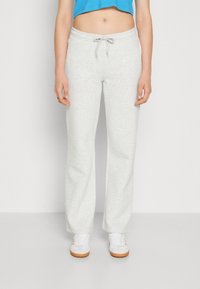 Lys grå joggebukser med løs passform, snøring i midjen og myk tekstur, kombinert med hvite sneakers med oransje detaljer.