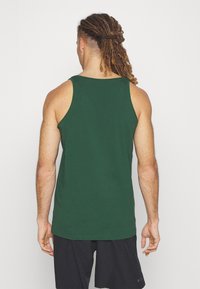 Top verde realizzato in cotone morbido, con scollatura rotonda e ampie aperture per le braccia. Design semplice con taglio dritto e senza fantasie.