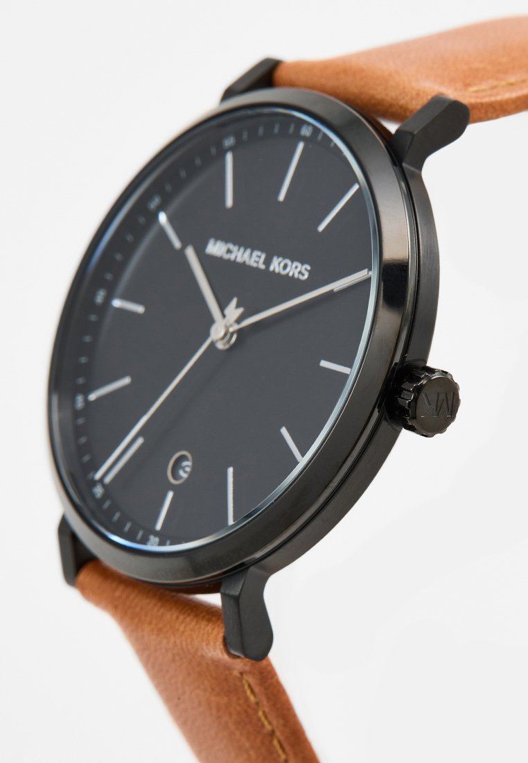 Zwarte horloge met een ronde wijzerplaat, dunne metalen behuizing, leren band in bruin, witte uurmarkeringen en logo op de positie van 12 uur. Kroon aan de zijkant.
