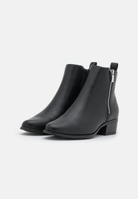 Bottines noires en cuir lisse, avec une fermeture éclair latérale, un bout pointu et un petit talon bloc. Design épuré sans motifs.