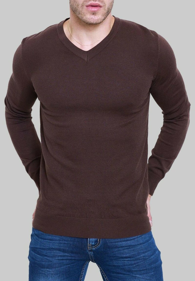 Pull en V marron à manches longues, fabriqué dans un matériau lisse, avec une silhouette ajustée et des poignets et ourlet côtelés. Porté avec un jean bleu.