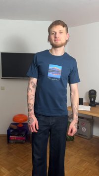 Navy blue cotton t-shirt with a mountain graphic at center. Paired with dark denim flared pants. Model stands in a minimalistic room.