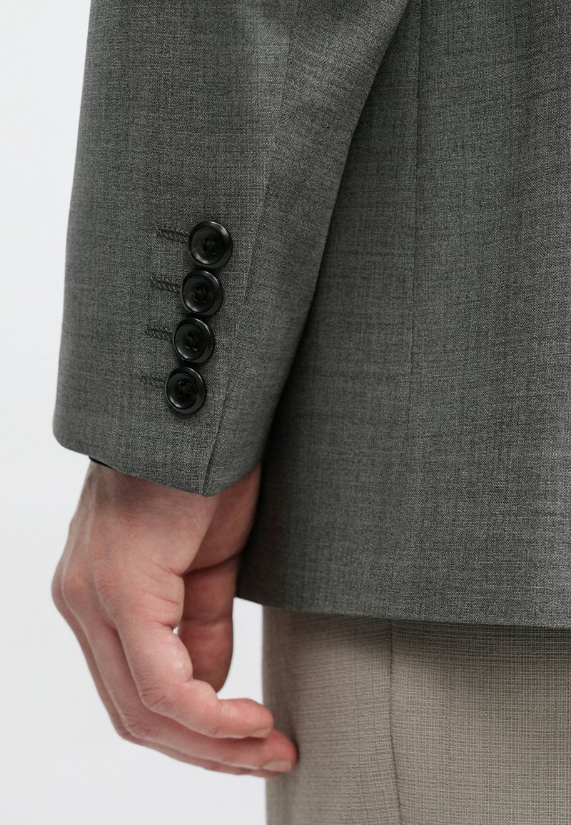 Gray textured fabric jacket sleeve features four black buttons and contrasting stitching, accentuating a tailored design.