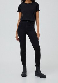 Camiseta de algodón negra combinada con jeans skinny negros de tiro alto y botas de tobillo. Textura suave, diseño ajustado y esquema de color monocromático.