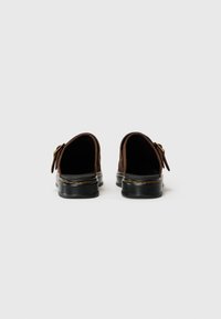 Scarpe slip-on in pelle marrone con talloni arrotondati, suole in gomma nera, dettagli in cucitura gialla e accenti decorativi a forma di fibbia.