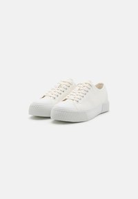 White canvas sneakers with rubber sole, round toe, and lace-up design. Textured sole with horizontal grooves, simple and minimalistic style.