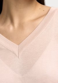 Helles rosa Strickpullover mit V-Ausschnitt, der eine glatte Textur und gerippte Kanten um den Hals aufweist. Nahaufnahme der Textildetails.