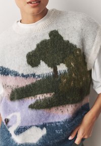 Pull en tricot arborant un motif paysager avec un arbre vert et un cygne blanc, mêlant des nuances de beige, rose, bleu et vert. Texture douce.