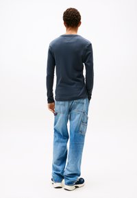 Granatowa koszulka z długim rękawem i okrągłym dekoltem, zestawiona z jasnobłękitnymi, luźnymi dżinsami z wieloma kieszeniami oraz akcentami w kolorach czerwonym, białym i niebieskim.