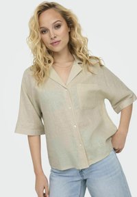 Beige linned skjorte med korte ærmer, knaplukning og krave, samt en frontlomme. Skjorten har en løs pasform og en subtil tekstur.
