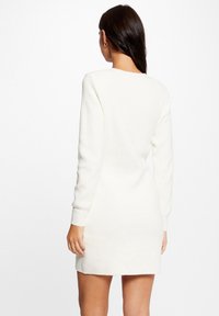 Abito in maglia color crema con maniche lunghe, tessuto texture, lunghezza sopra il ginocchio e scollatura rotonda. Nessun motivo o dettaglio in metallo visibile.