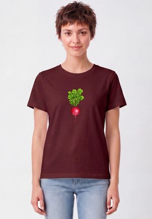Junge Frau trägt ein bordeauxfarbenes T-Shirt mit einer bunten Rettich-Grafik in der Mitte vorne, kombiniert mit hellblauen Jeans.