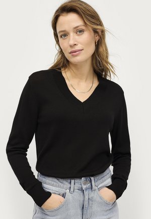 Black v-neck sweater with long sleeves, knit texture, and ribbed cuffs, paired with light blue high-waisted jeans.
