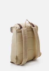 Sac à dos beige avec un dos texturé en maille, des accents en cuir brun et des bretelles réglables. Il possède une poignée supérieure et une construction rembourrée.