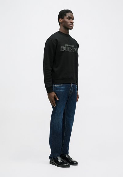 Zwarte sweatshirt met verhoogd "Ducati" logo, gecombineerd met donkerblauwe spijkerbroeken. Model draagt zwarte leren schoenen. Eenvoudige, casual stijl.