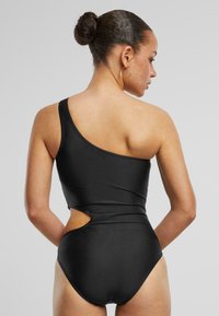Maillot de bain noir une pièce avec un design épaule dénudée, détail découpé sur le côté et texture lisse.