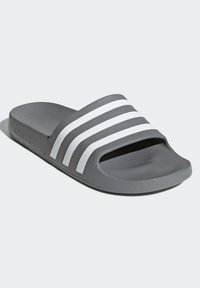 Pantofole grigie in materiale sintetico con superficie strutturata. Presentano tre strisce bianche orizzontali sulla parte superiore.
