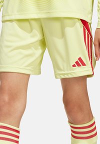 Geel sportshorts met rode zijstrepen, gemaakt van lichtgewicht, glad materiaal. Gecombineerd met witte en rode gestreepte sokken.